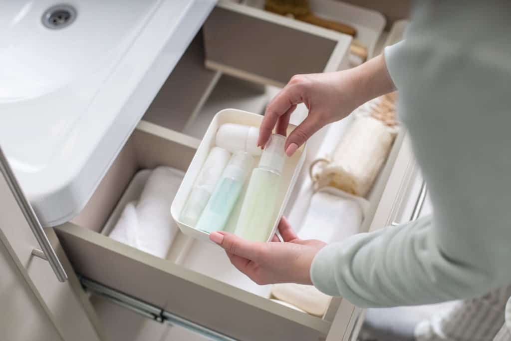 A woman pulling out toiletries from a drawer under the bathroom sink 